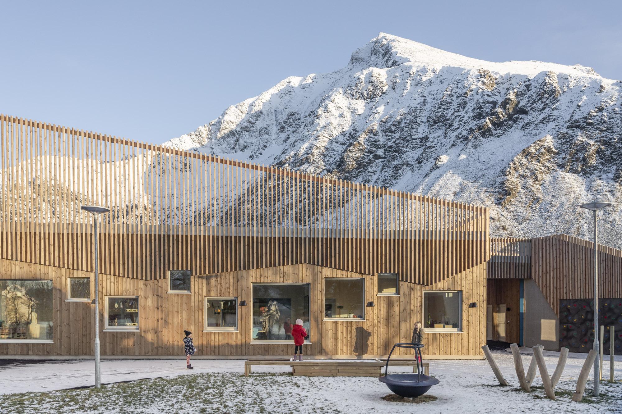 Skolefasade med spiler på taket og massivtre. Fjellandskap. Foto