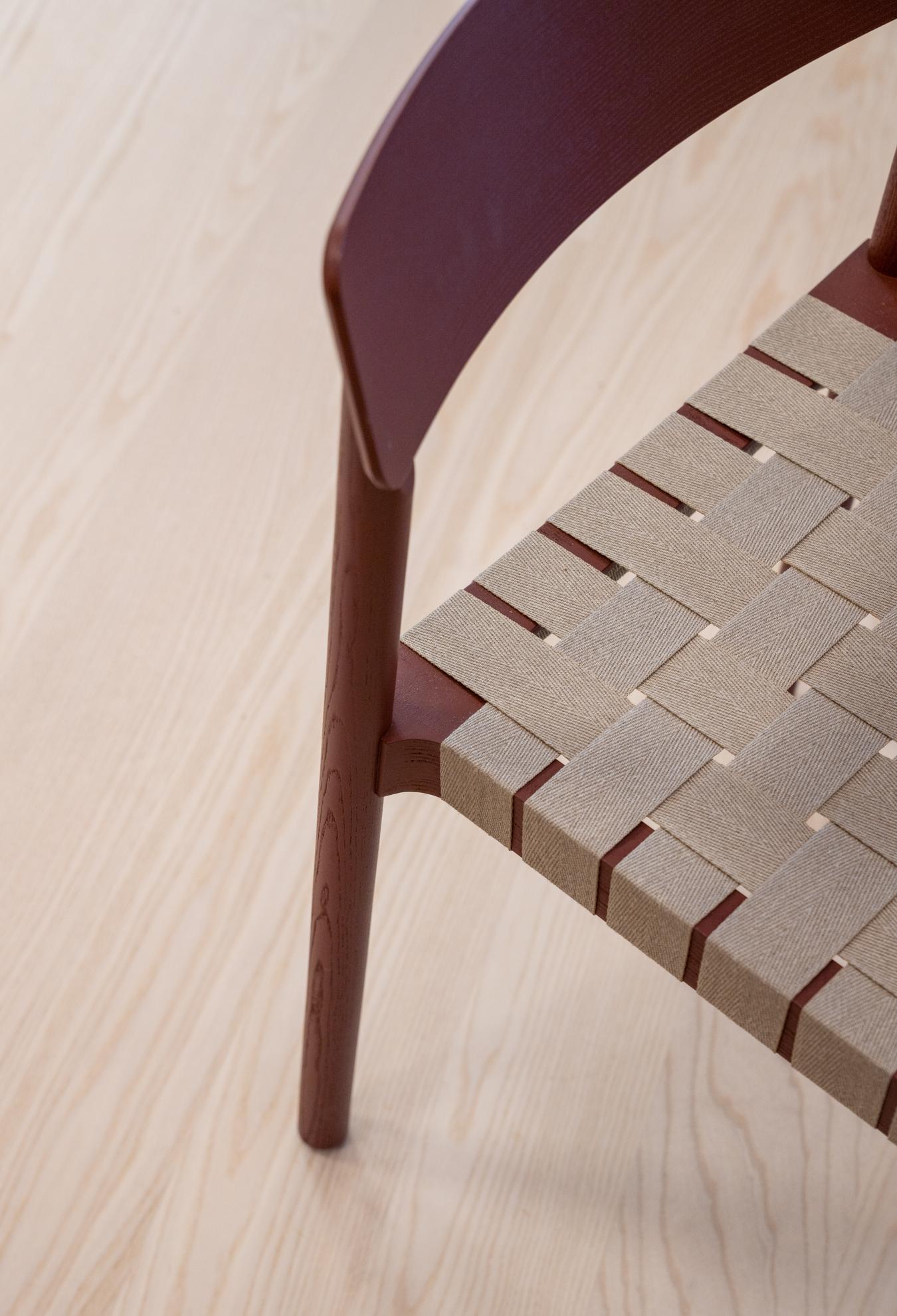 Detalbilde av stol i brunt stoff og røde detaljer. Foto